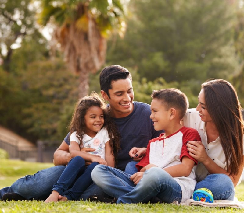 Happy,Young,Hispanic,Family,Sitting,Together,On,The,Grass,In
